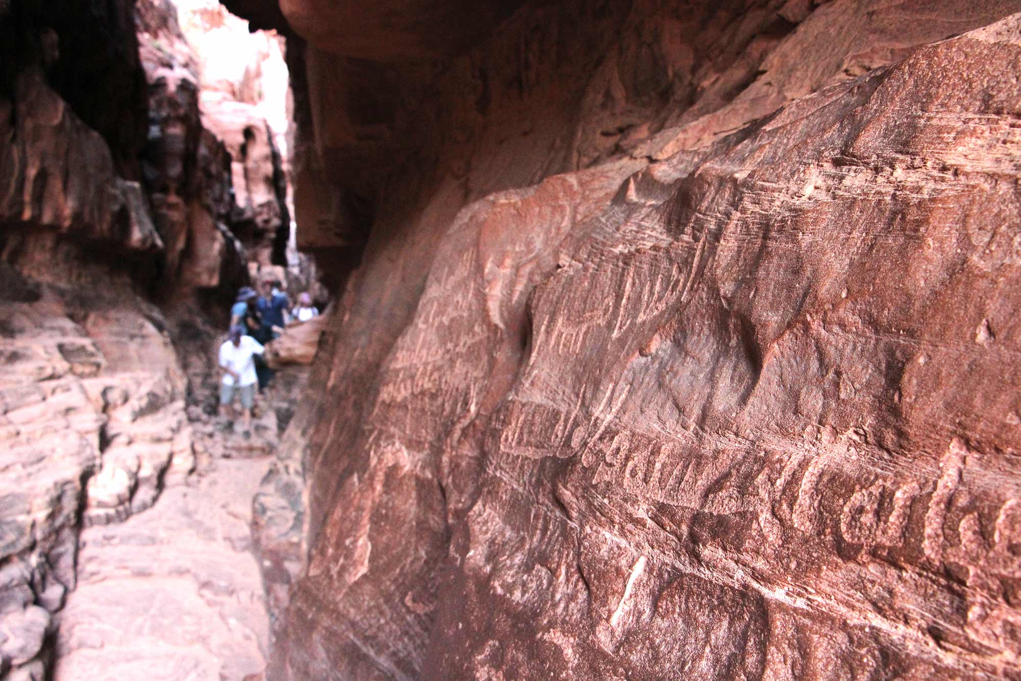 Tourists admiring the proto-Arabic writing and other ancient art carved into the walls of Khazali Canyon in Wadi Rum, Jordan