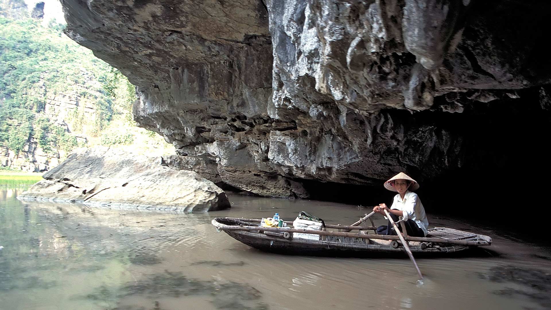 Woman rowing a boat Ngo Dong River exiting Hang Ca Cave in the limestone karst mountains, Tam Coc, Ninh Binh, Vietnam