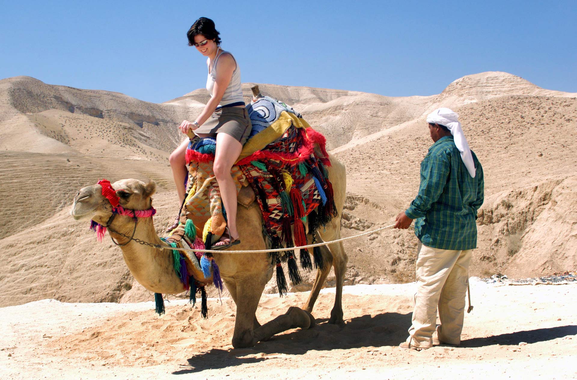 Tourist rides a camel of a Bedouin man in the Desert