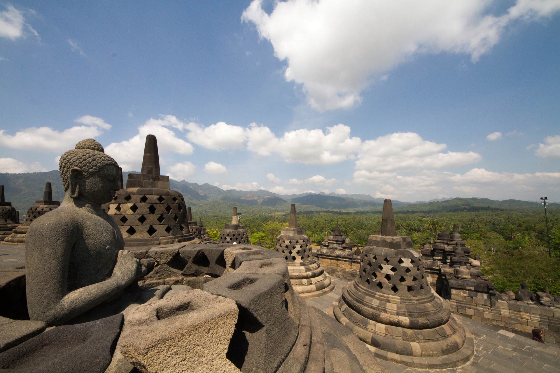 Buddha statue with the hand position of dharmachakra mudra  amidst the latticed stone stupas containing Buddha statues on the upper terrace, Borobudur Temple Compounds, Central Java, Indonesia