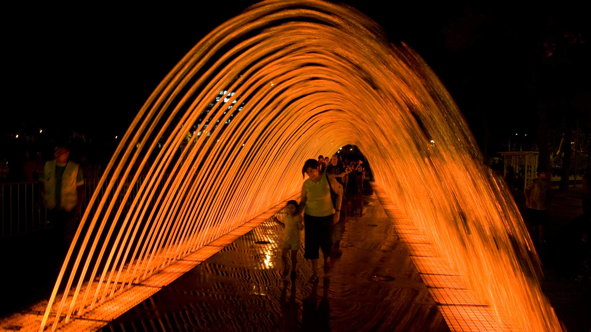 People walking through the Fuente Túnel de la Sorpresas (Tunnel of Surprises Fountain) in Parque de la Reserva at night, Lima